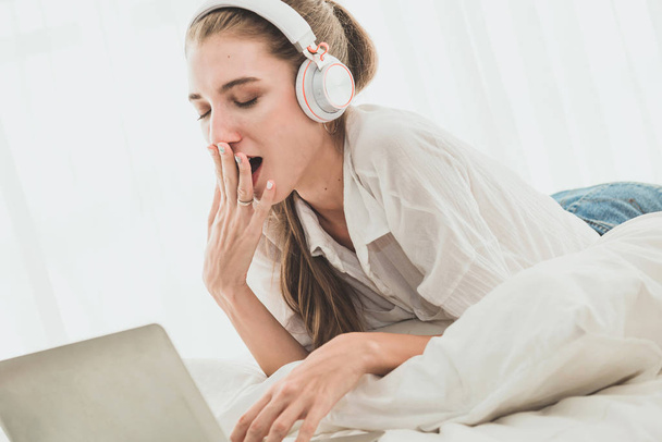 Beautiful woman yawning front of laptop computer while laying on - Valokuva, kuva