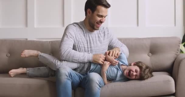 Happy loving dad tickling child son laughing playing on sofa - Filmati, video