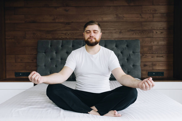 Handsome caucasian man meditating and being mindful on his bed in bedroom - Photo, image