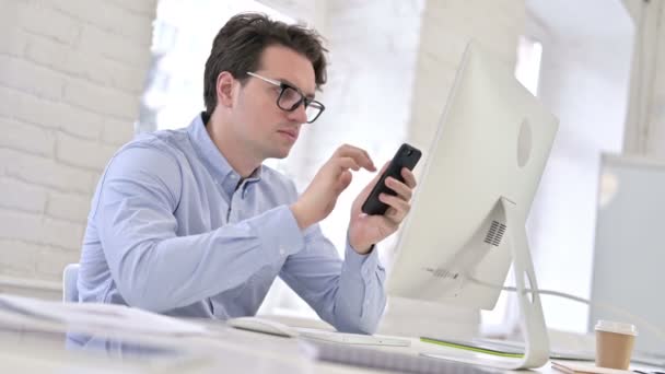 Серьезный рабочий молодой человек с помощью смартфона в офисе
 - Кадры, видео