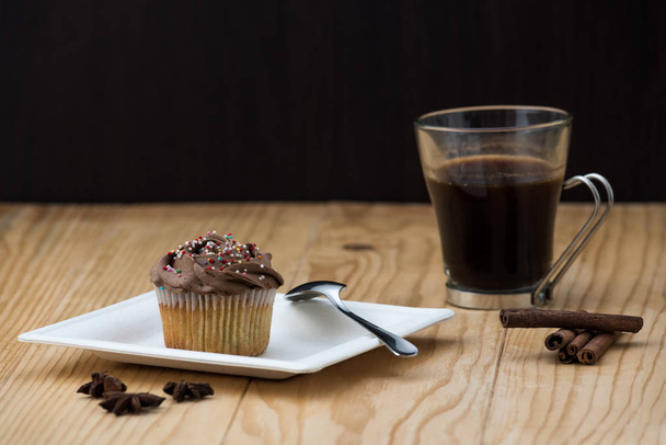 Muffinka czekoladowa z gorącą filiżanką kawy, paluszkami cynamonowymi i gwiazdkami Anise na drewnianym stole - Zdjęcie, obraz