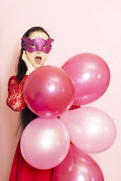 Young pretty woman in masquerade mask holding festive air balloons. Portrait of happy 20s middle-eastern female celebrating valentines day, birthday, party - Photo, Image
