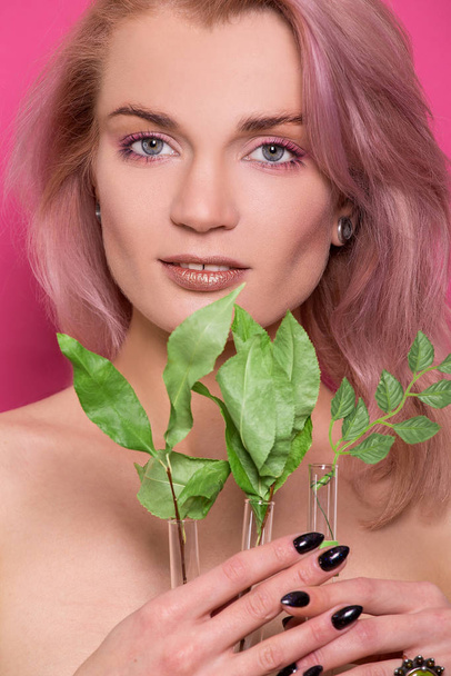Shiny golden make-up on a beautiful young European model girl holding a twig with green leaves in hand isolated on an pink background in the photo studio - Foto, immagini