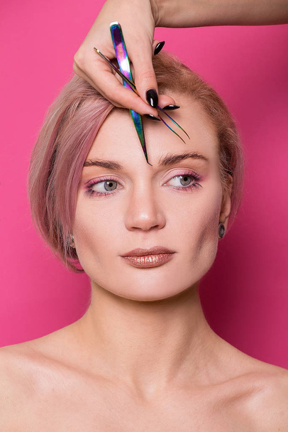 Close-up of a beautiful girl of European appearance holds in her hand tweezers for eyebrows near the face in the studio isolated on a pink background - Foto, Imagen