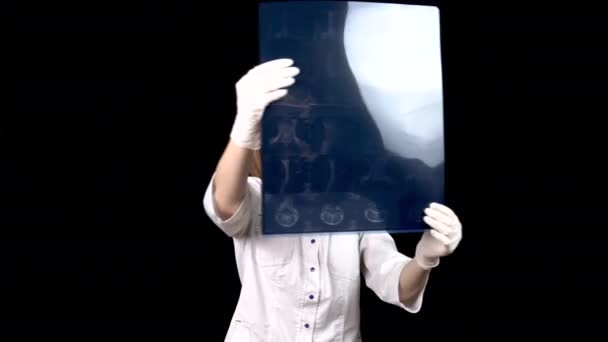 Een jonge vrouwelijke arts controleert de resultaten van een MRI scan van een wervelkolom. Een vrouw onderzoekt een MRI-beeld en toont dan een duim naar beneden. Negatief MRI resultaat. Op een zwarte achtergrond. - Video