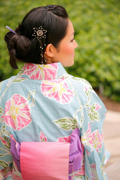 jong aziatisch meisje in een traditionele kimono met een ventilator in een natuurlijke en pittoreske outdoor omgeving - Foto, afbeelding