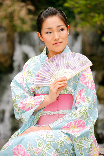Joven chica asiática en un kimono tradicional con un ventilador en un entorno natural y pintoresco al aire libre
 - Foto, Imagen