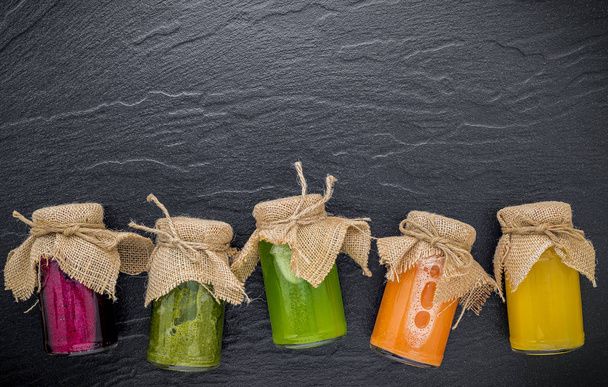 Színes, egészséges turmixok és gyümölcslevek palackban sötét kövön  - Fotó, kép