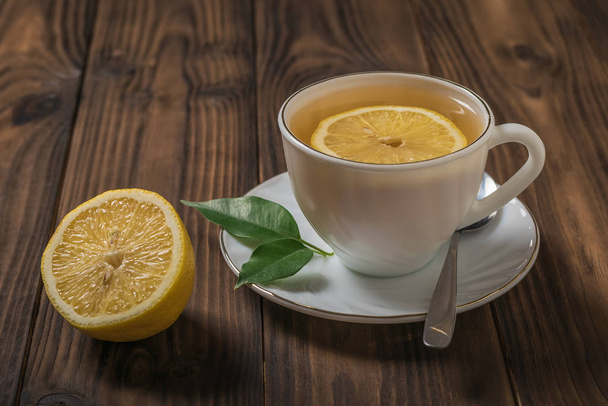 Čaj s citronovými plátky v bílém poháru na dřevěném stole. - Fotografie, Obrázek