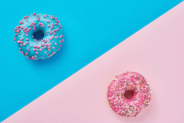 Két fánk pasztell rózsaszín és kék háttérrel. Minimalizmus kreatív ételek összetétele. Lapos fektetési stílus - Fotó, kép