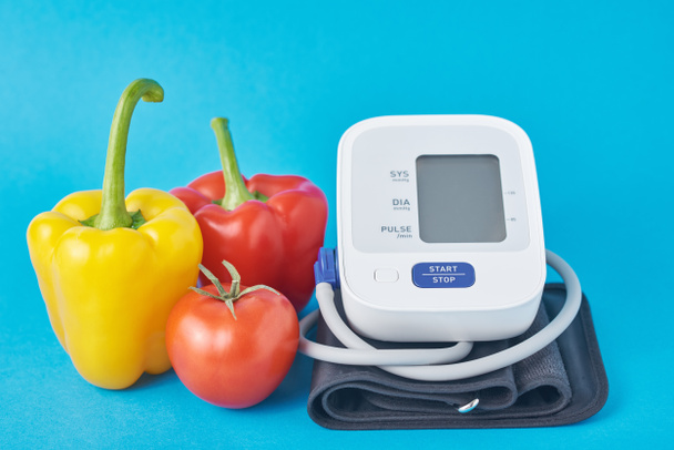 Digitale bloeddrukmeter en verse groenten op een blauwe achtergrond. Gezondheidszorgconcept - Foto, afbeelding