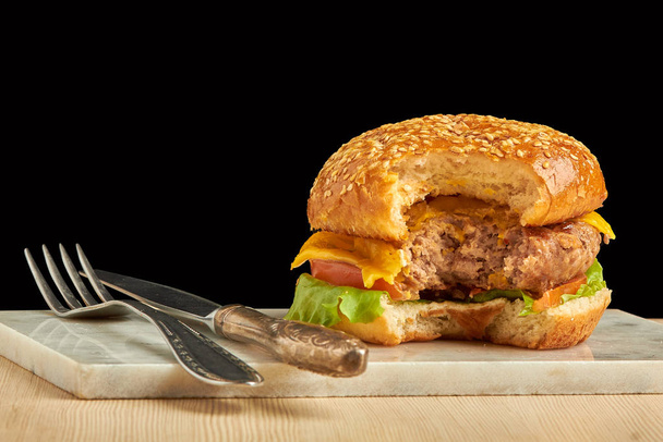 Craft burger with fork and knife on black background. Cheeseburger on plate. - Foto, imagen