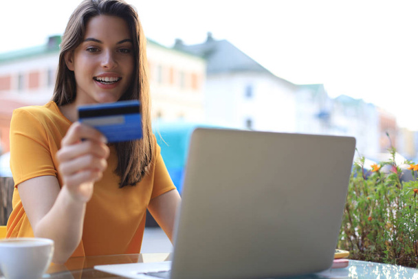 Happy natural brunette using credit card and laptop in cafe outdoors. - Foto, Bild