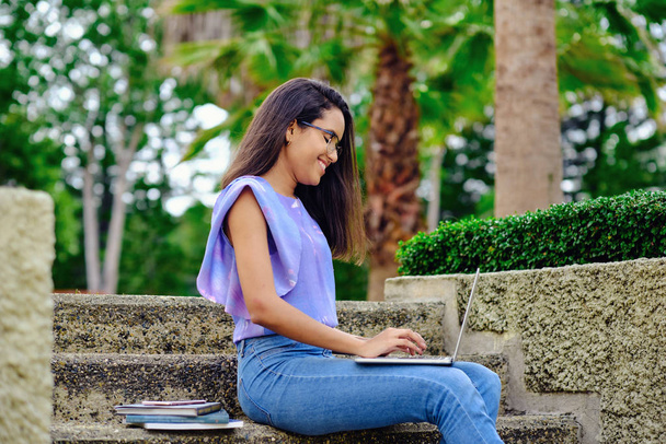 glimlachende student meisje voorbereiding voor examens buiten met computer - Foto, afbeelding