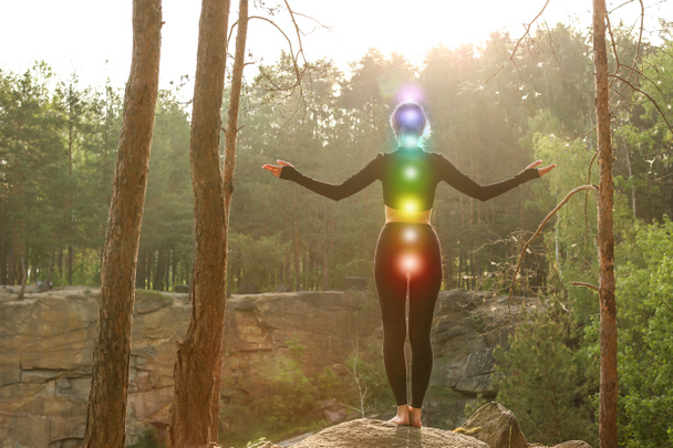 Woman with colorful chakras meditating in forest - Photo, Image