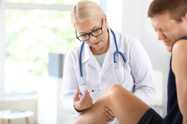 Kypsä lääkäri antaa urheilijalle nivelkipu injektio klinikalla
 - Valokuva, kuva