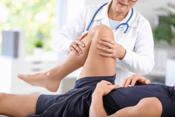 Зрелый врач осматривает спортсмена с болью в суставах в клинике
 - Фото, изображение