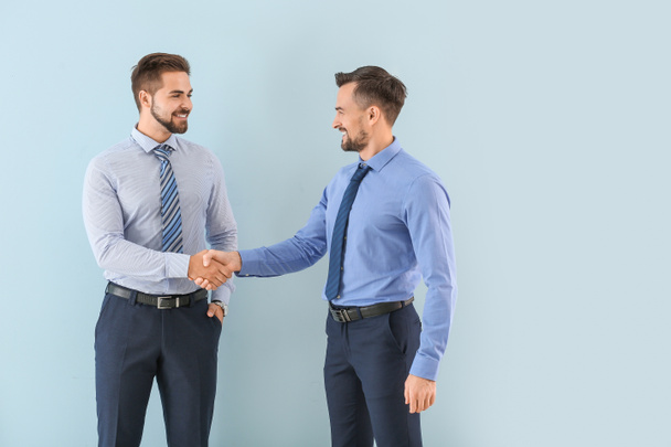 Young businessmen shaking hands on color background - 写真・画像