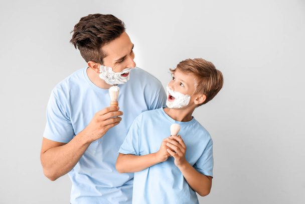 Забавный отец и его маленький сын бреются на сером фоне
 - Фото, изображение