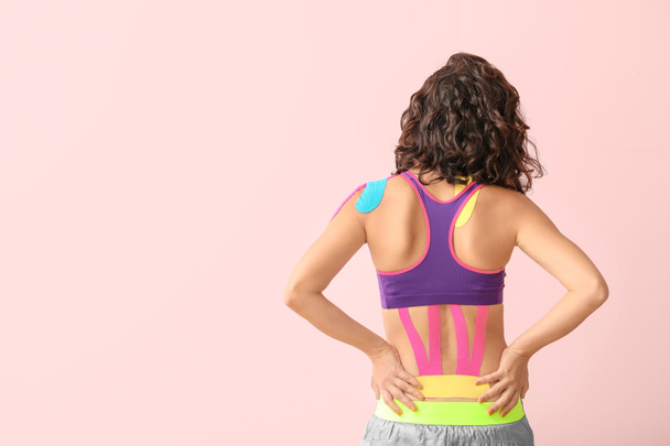 Αθλητική γυναίκα με ταινία physio εφαρμόζεται στο κάτω μέρος της πλάτης με φόντο το χρώμα - Φωτογραφία, εικόνα