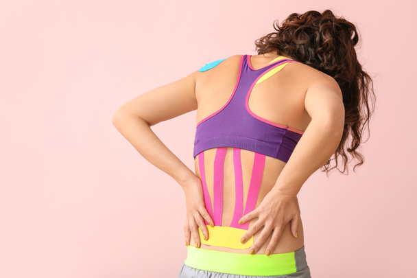 Mulher esportiva com fita fisiológica aplicada na parte inferior das costas contra fundo de cor
 - Foto, Imagem
