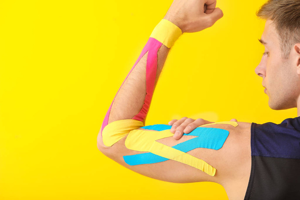 Sportovní muž s fyziologickou páskou aplikovanou na paži proti barevnému pozadí - Fotografie, Obrázek
