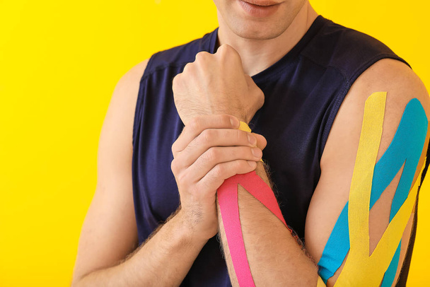 Sportieve man met fysioband aangebracht op arm tegen kleur achtergrond, close-up - Foto, afbeelding