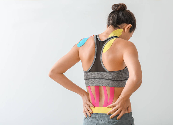 Sportos nő fiziofilmmel ragasztószalaggal a hátán, világos háttér mellett - Fotó, kép