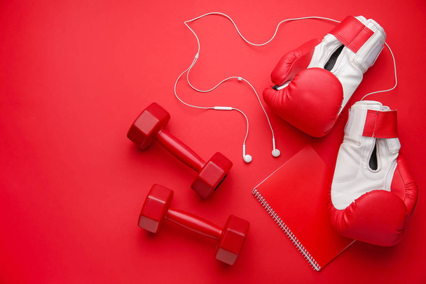 Dumbbells with boxing gloves, earphones and notebook on color background - Photo, Image