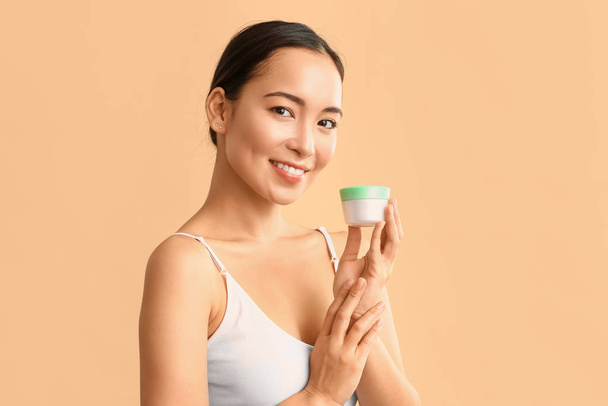 Beautiful Asian woman with jar of cream on color background - Photo, Image