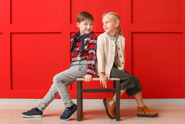 Söpöt pikkulapset syksyn vaatteissa istumassa lähellä väriseinää
 - Valokuva, kuva
