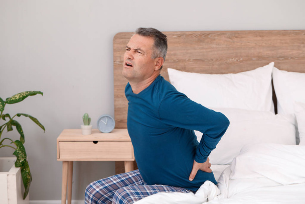 Mature man suffering from back pain in bedroom - Photo, Image