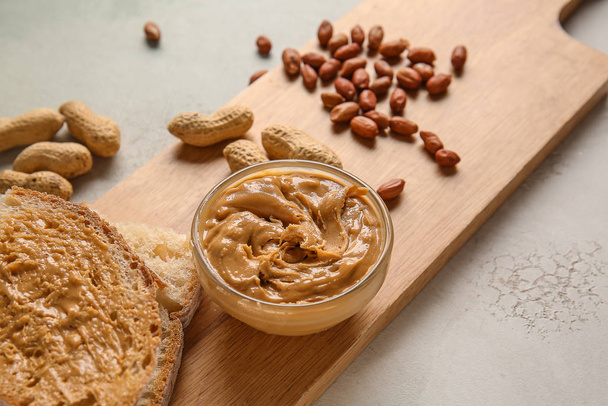 Board with fresh bread and tasty peanut butter on white background - Fotó, kép