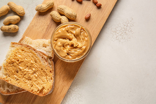Board with fresh bread and tasty peanut butter on white background - Zdjęcie, obraz