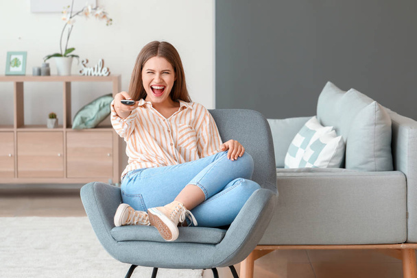 Happy woman watching TV while sitting in armchair at home - Photo, image
