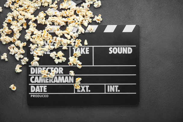 Tasty popcorn with movie clapper on dark background - Photo, Image