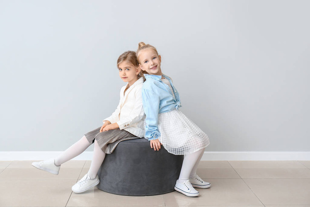 Lindas niñas en ropa de otoño sentadas cerca de la pared gris
 - Foto, imagen