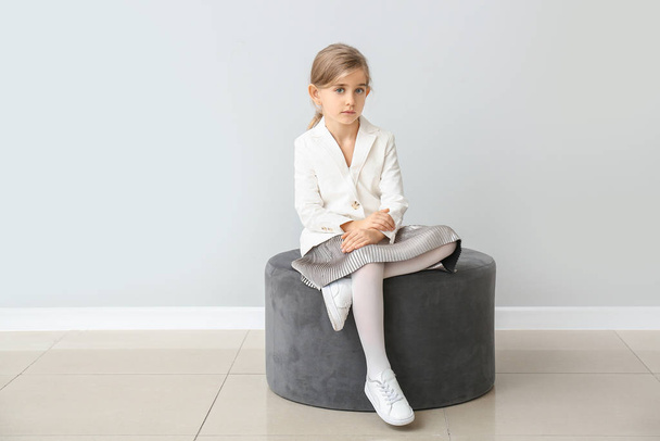 Cute little girl in autumn clothes sitting near grey wall - Foto, imagen