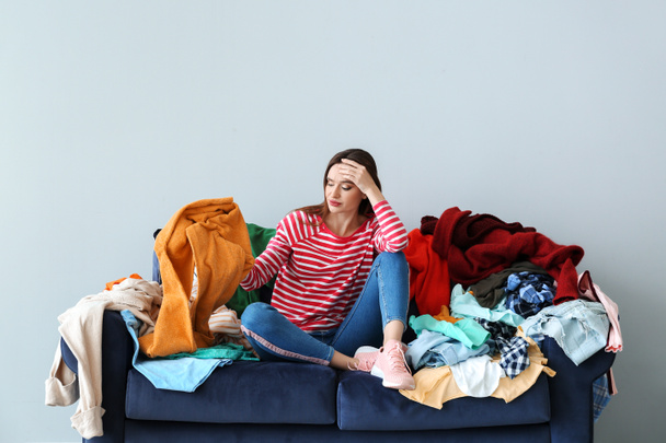 Sad woman with heap of clothes on sofa indoors - Fotó, kép