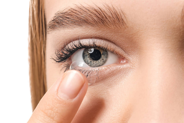 jonge vrouw zetten in contact lens op witte achtergrond, close-up - Foto, afbeelding