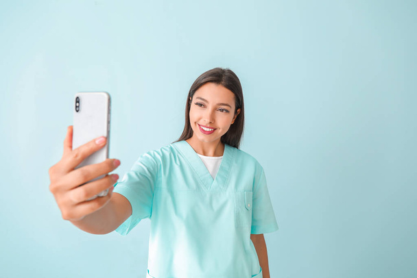 Young nurse taking selfie on color background - Foto, imagen