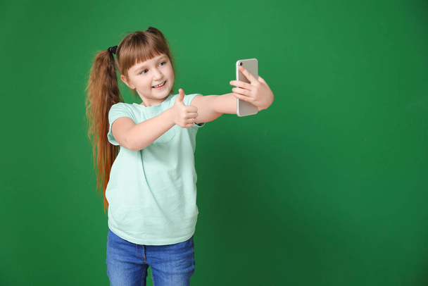 Little girl taking selfie on color background - 写真・画像