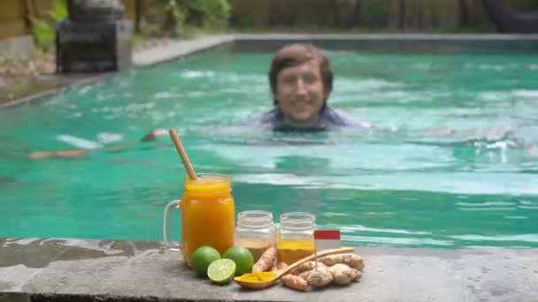 A young man drinks the national Balinese drink Jamu swimming in the swimming pool - Кадри, відео