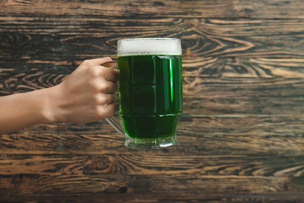Γυναικείο χέρι με κούπα πράσινη μπύρα για την Ημέρα του Αγίου Πατρικίου σε ξύλινο φόντο - Φωτογραφία, εικόνα
