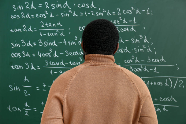 Profesor de matemáticas afroamericano cerca de pizarra en el aula
 - Foto, imagen