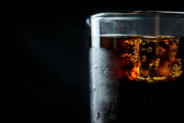 Soda in a glass on a black background with ice cubes and drops - Фото, изображение