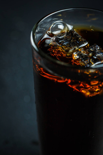 Soda in a glass on a black background with ice cubes and drops - Fotó, kép