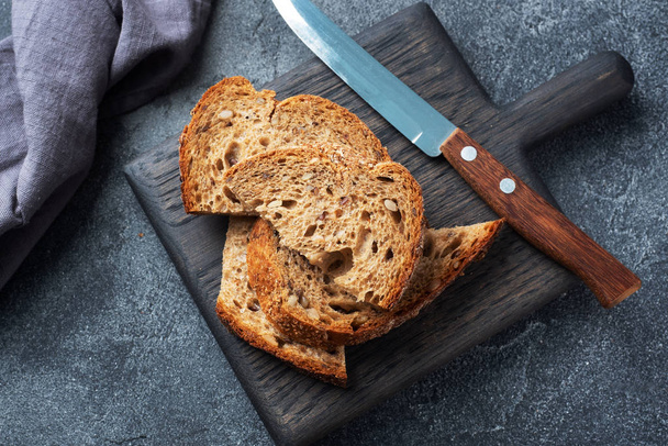 Slices of wholegrain bread on a wooden cutting Board. Dark concrete background. - Fotografie, Obrázek