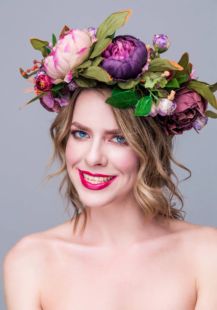 mooie jonge vrouw model met heldere bloemen op haar hoofd op grijze achtergrond - Foto, afbeelding