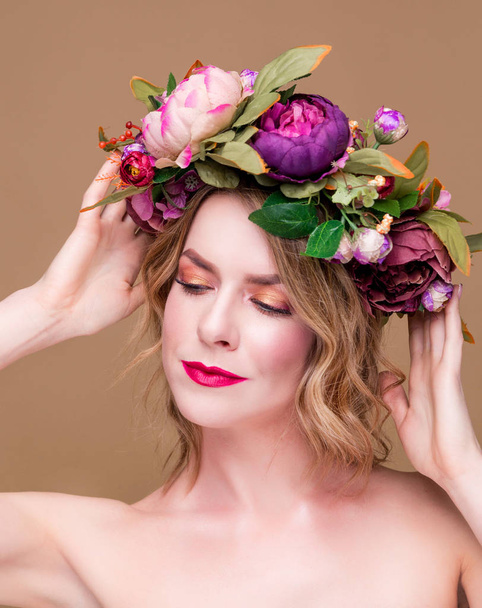 όμορφη νεαρή γυναίκα μοντέλο με φωτεινά λουλούδια στο κεφάλι της στο φόντο χρώμα ώχρα - Φωτογραφία, εικόνα